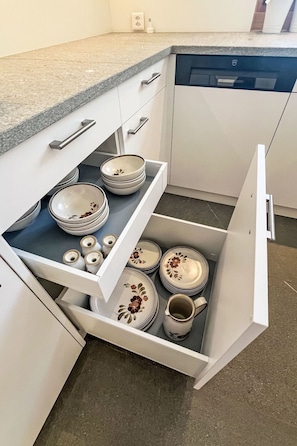 A kitchen with white cabinets, a countertop, and a drawer with stacked plates and bowls. - Panorama - Chesa Roseg ÖV inklusive by Interhome (Pontresina)