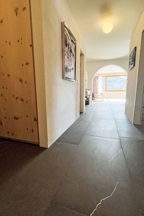 A hallway with a wooden door, a framed picture on the wall, and a tiled floor. - Panorama - Chesa Roseg ÖV inklusive by Interhome (Pontresina)