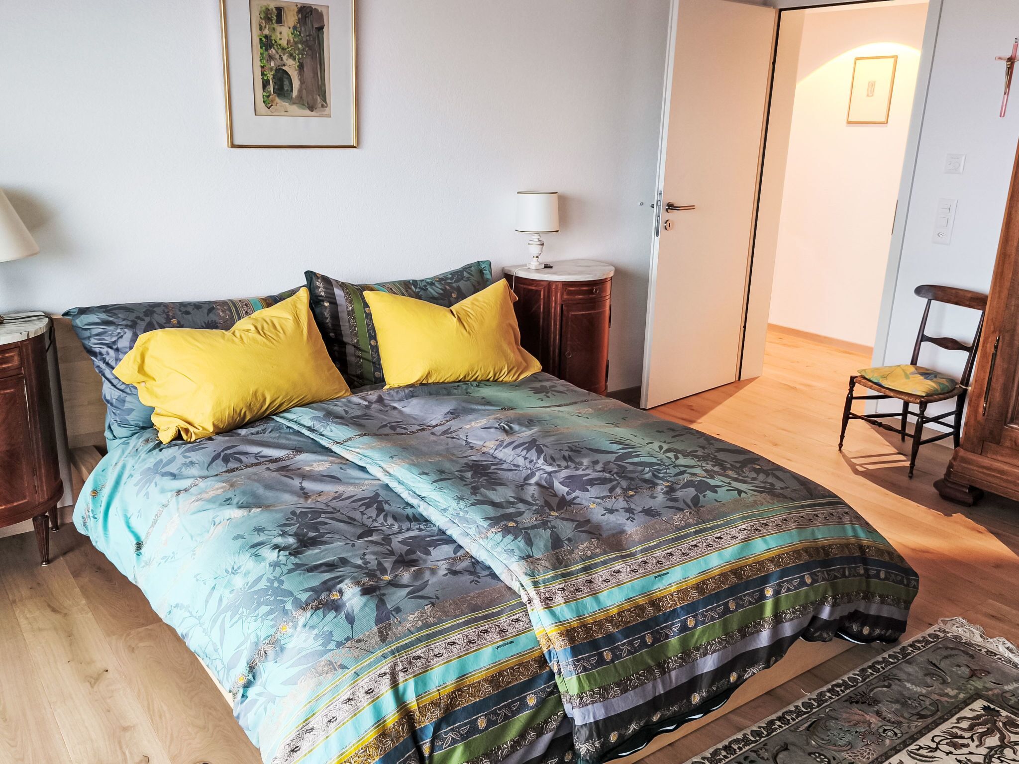 Ein Schlafzimmer mit einem Bett, einem Nachttisch, einer Lampe, einem Sessel und einer Tür.