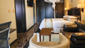 A hotel room with a bed, a leather sofa, a small round table, a TV, and a mosquito net. - Annavilla7 Lilongwe Hotel (Lilongwe)
