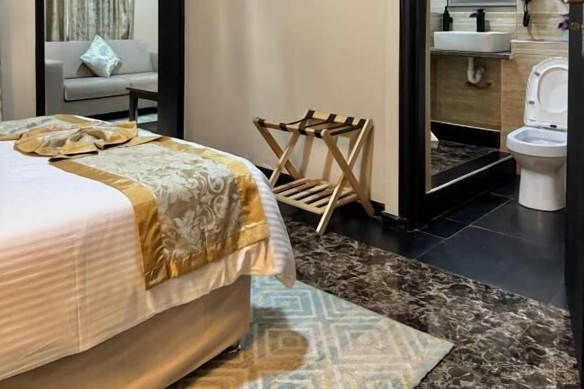 Habitación de hotel con cama, televisor, una mesita pequeña, una silla y un baño visible a través de una puerta abierta.