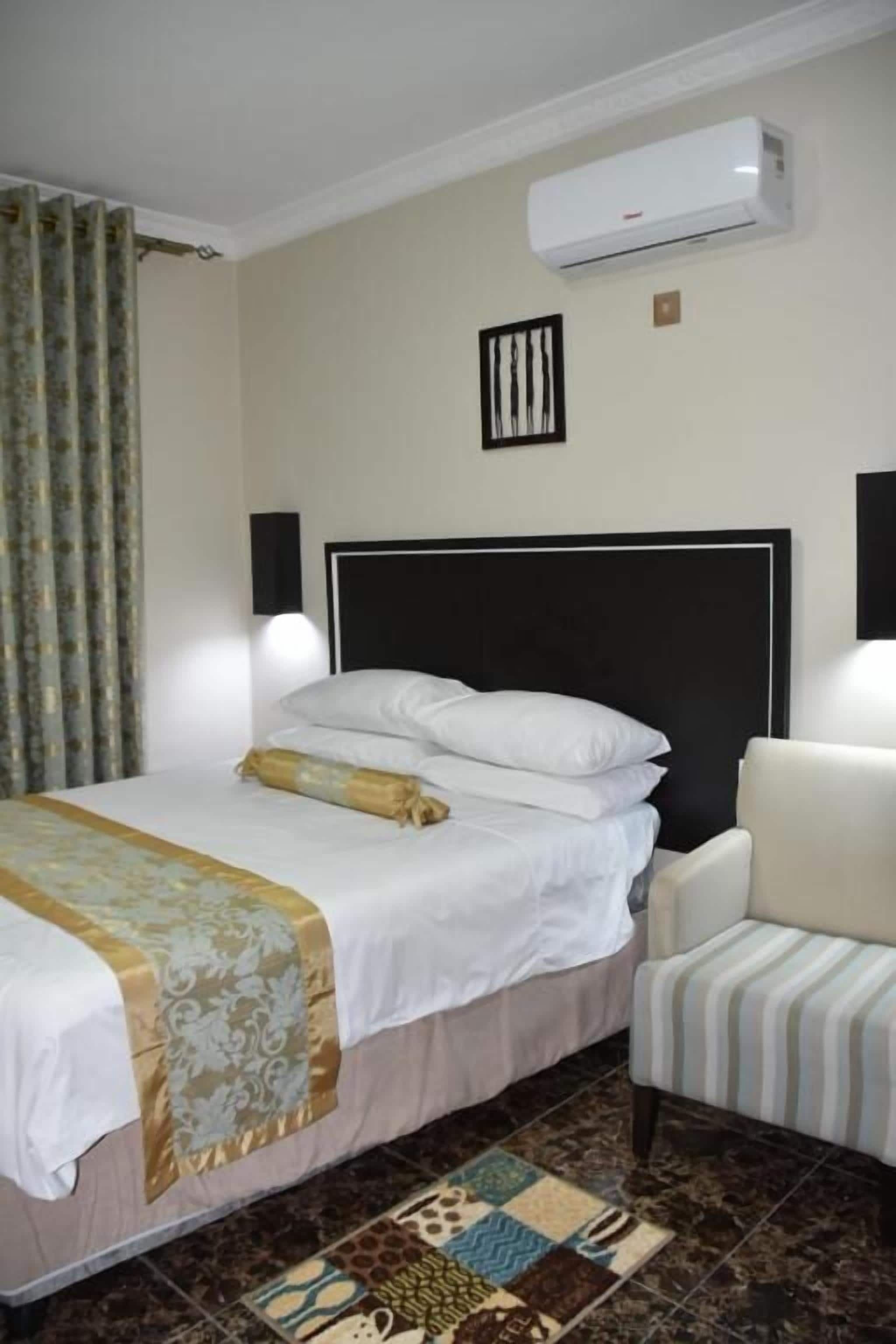 Une chambre d’hôtel avec un lit, une chaise, un appareil de climatisation et un tapis à motifs.