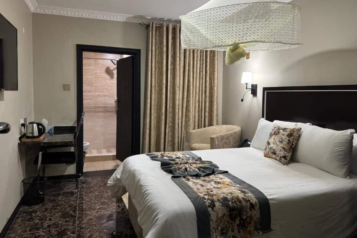 Habitación de hotel con cama, escritorio, silla, lámpara colgante y vista a través de una puerta.