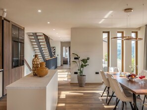Eine moderne Küche mit einer Holztreppe, einem Essbereich mit Tisch für zwei Personen und einer großen Kübelpflanze.