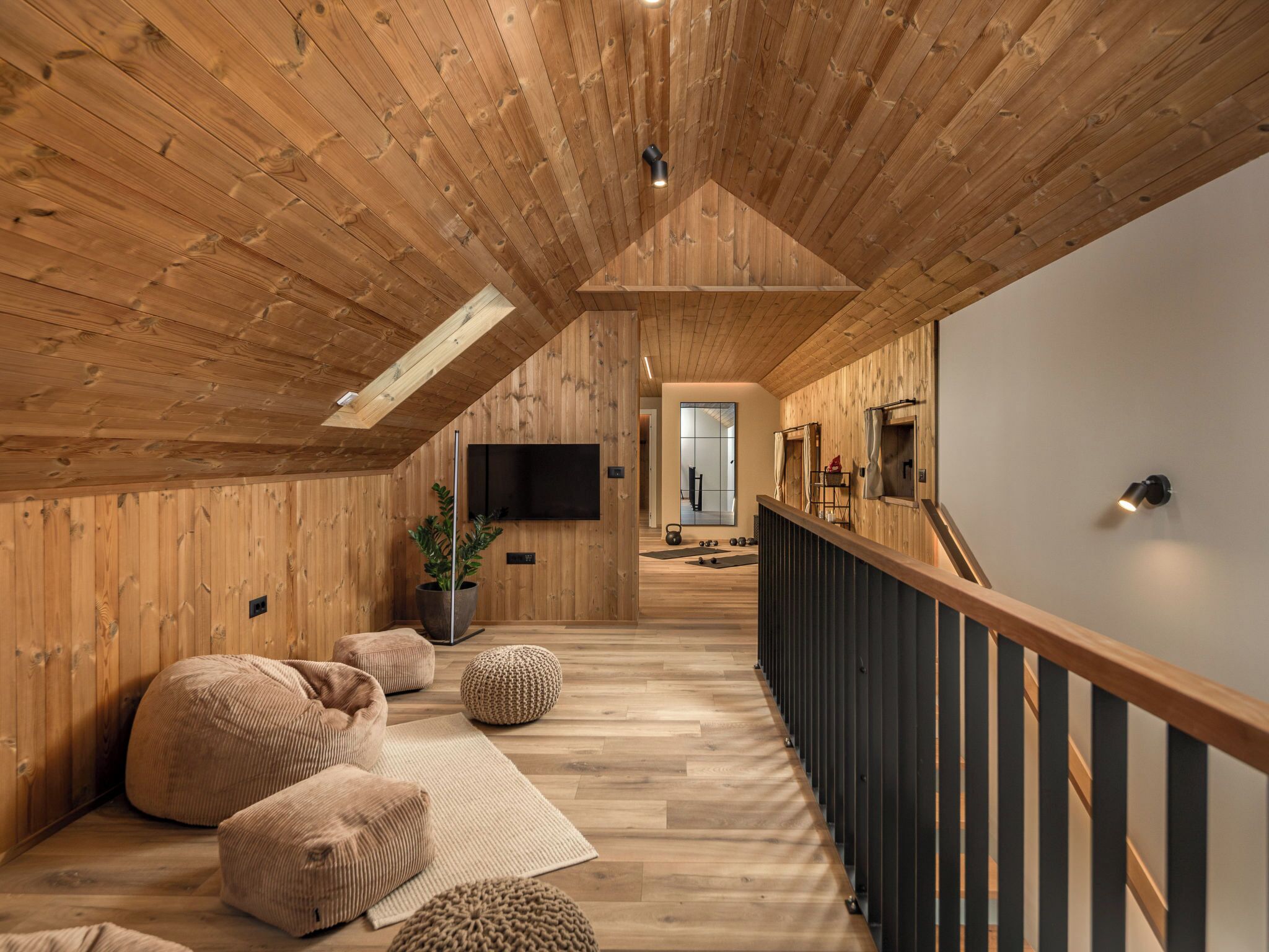 A wooden interior with a sloped ceiling, a TV mounted on the wall, and a staircase on the right.