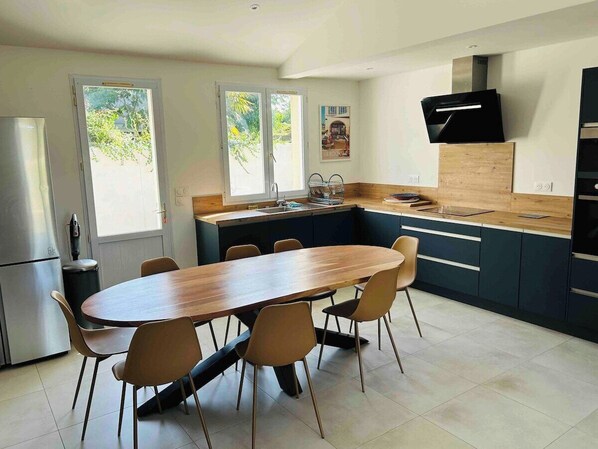 A modern kitchen with a wooden dining table and chairs, a built-in oven, and a large window.
