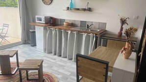 A compact kitchen with a microwave, sink, and wooden countertop. There is a dining area with a table and chairs, and a potted plant on a side table. - Villa Mathéo swimming pool La Rochelle Fun et Calm (Aytré)