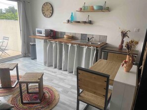 Eine kompakte Küche mit Mikrowelle, Spüle und Holzarbeitsplatte. Es gibt einen Essbereich mit Tisch und Stühlen, und eine Zimmerpflanze auf einem Beistelltisch.