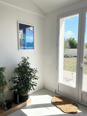 A room with a large window, a poster on the wall, a potted plant, and a woven rug.