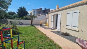 A residential area with a pathway leading to a building with white shutters, a small garden, and a colorful play structure. - Villa Mathéo swimming pool La Rochelle Fun et Calm (Aytré)