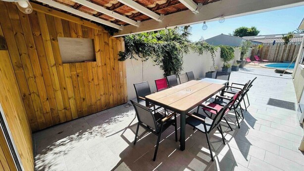 An outdoor patio with a wooden table and chairs, a ceiling fan, and a view of a swimming pool. - Villa Mathéo swimming pool La Rochelle Fun et Calm (Aytré)