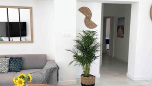 A modern living room with a sofa, a coffee table with sunflowers, a potted plant, and a round ottoman. - Villa Mathéo swimming pool La Rochelle Fun et Calm (Aytré)