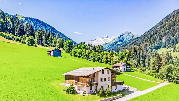 A two-story building with a sloped roof, situated on a green hillside with a clear sky.