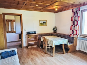 Een kamer met een houten bank, een tafel met een tafelkleed met patroon, een radiator en een raam met gordijnen.