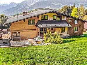 A two-story wooden house with a sloped roof, a covered porch, and a small outdoor seating area.