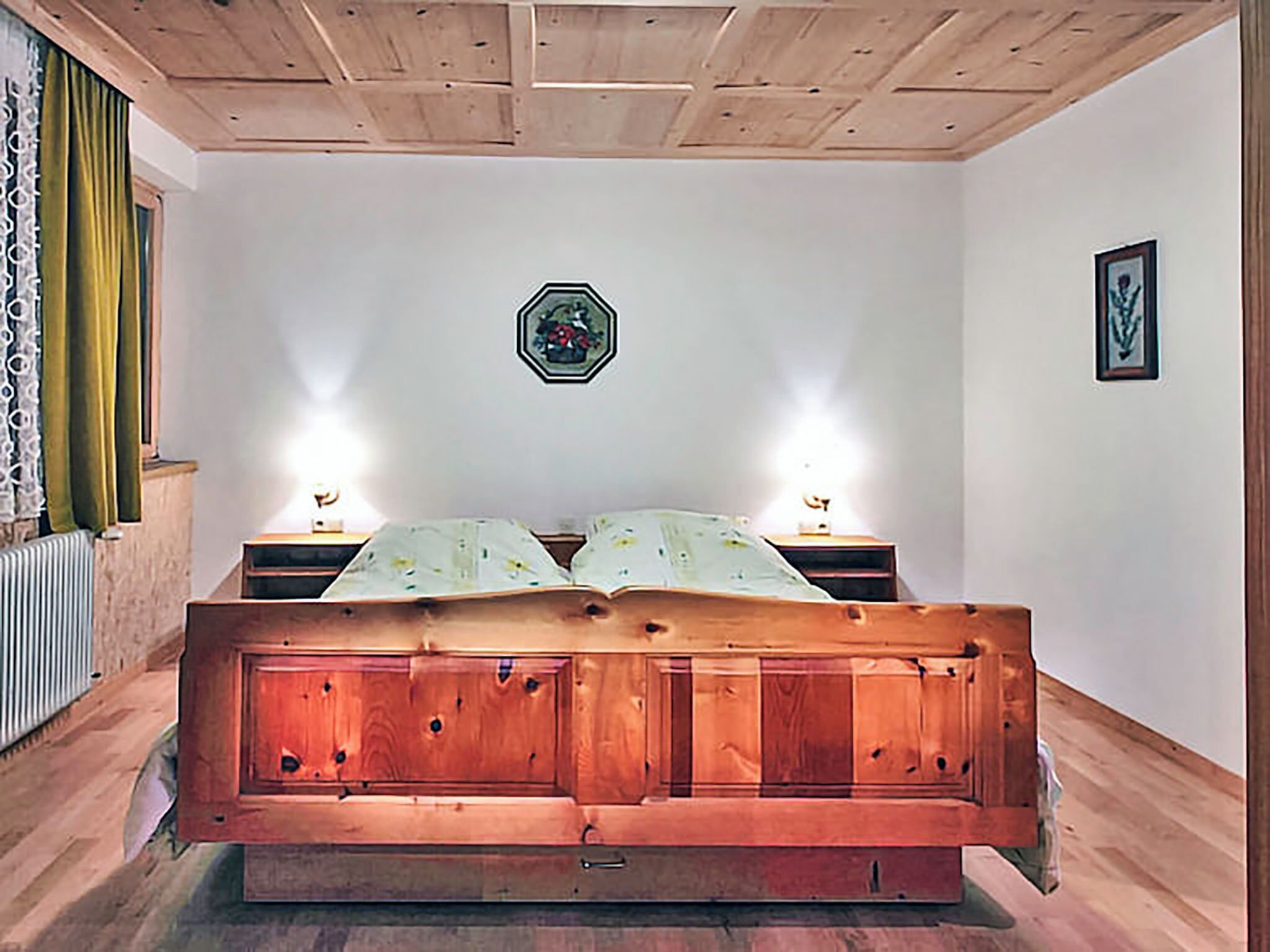 Un lit en bois, deux lampes de chevet, un radiateur et un tableau encadré au mur.