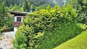 Una cabaña de montaña con un balcón de madera, rodeada de abundante vegetación y vistas a colinas boscosas.