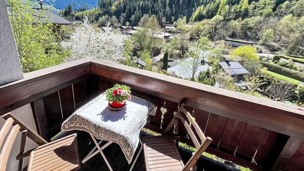 Un balcón con mesa y sillas, con vistas a un pueblo con casas y montañas.