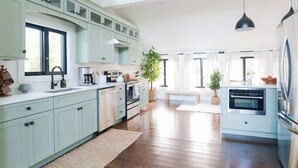 Een moderne keuken met lichtblauwe kastjes, een groot kookeiland, roestvrijstalen apparatuur en een hangende吊灯.