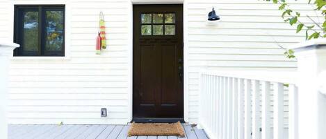 A white house with a dark brown front door, a small window, and a porch with a doormat.