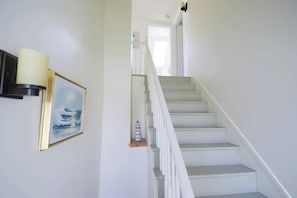 Eine Treppe mit weißen Geländern und Stufen, ein gerahmtes Bild an der Wand und ein kleines Regal mit einem dekorativen Gegenstand.