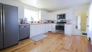 A modern kitchen with white cabinets, stainless steel appliances, and a wooden floor.