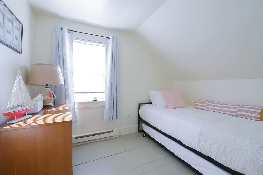 Ein Schlafzimmer mit Bett, Schreibtisch mit Lampe, einem Fenster mit Vorhängen und einer Heizung.