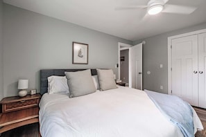 Une chambre à coucher comprenant un lit, une table de chevet, une lampe, un tableau encadré et un ventilateur de plafond.