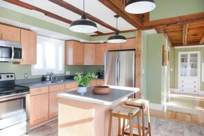 A kitchen with wooden cabinets, a central island, bar stools, a refrigerator, and pendant lighting. - Fully Updated Airy Historic Home in South Freeport (Freeport)