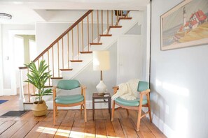 Una escalera con barandillas de madera, dos sillas de madera con cojines, una mesita con una lámpara y una planta en maceta.