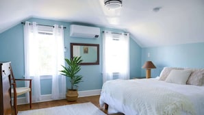 Een slaapkamer met een bed, een stoel, een bloempot en een lamp.