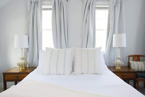 A neatly made bed with striped pillows, two bedside lamps, and a wooden nightstand. - Fully Renovated "Saltbox" Home in Boothbay (Boothbay)