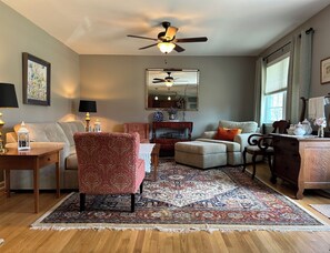 Ein Wohnzimmer mit Deckenventilator, großem Spiegel, gemustertem Teppich und Couchtisch aus Holz.