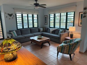 Ein Wohnzimmer mit Sofa, Couchtisch, gemustertem Sessel, Stehlampe und Deckenventilator.