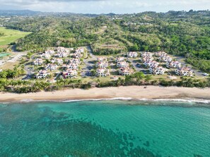 Ein Luftbild eines Küstenresorts mit Strandvillen, klarem türkisfarbenem Wasser und üppiger Vegetation.