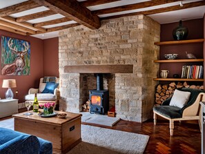 Ein gemütliches Wohnzimmer mit Kamin aus Stein, Holzbalken, einer Couch, einem Couchtisch und einem Bücherregal.