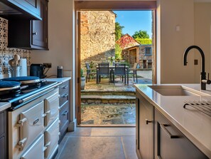 Eine Küche mit Steinwand, ein Essbereich mit Stühlen und Tisch sowie ein Blick auf ein Steinhaus im Freien.
