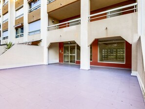 A spacious outdoor area with a tiled floor, a glass entrance, and a building with multiple floors and balconies. - Les Regates by Interhome (Hyères)