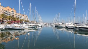 Ein Yachthafen mit zahlreichen Segelbooten, die in ruhigem Wasser vor Anker liegen, umgeben von Gebäuden und Palmen.