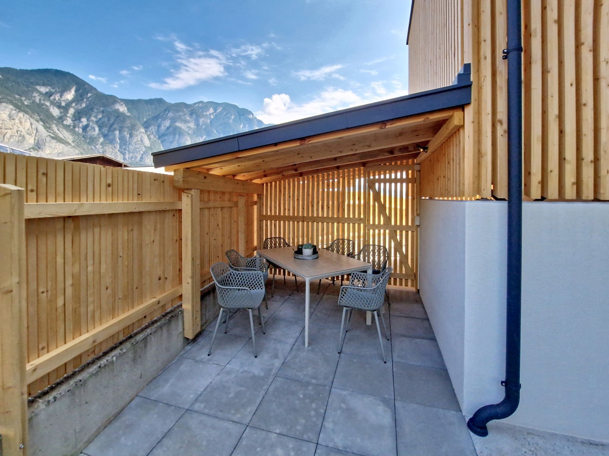 Une terrasse extérieure avec une table et des chaises, une clôture en bois et une vue sur les montagnes.