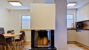 Une cuisine moderne dotée d’un poêle à bois encastré, d’un coin repas avec des chaises et d’un plan de travail équipé d’appareils électroménagers.
