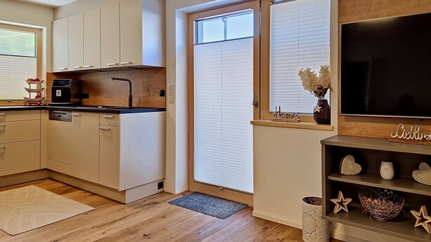 Une cuisine moderne avec des meubles en bois, un four encastré, un plan de travail noir et une fenêtre avec des stores.