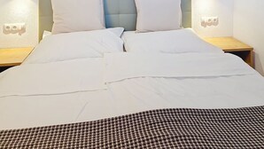 Un lit bien fait, avec du linge de lit blanc, un plaid à carreaux au pied du lit et deux lampes de chevet de chaque côté.