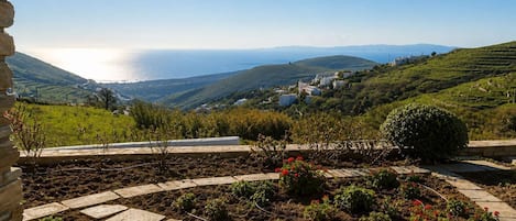 A stone pathway leading to a garden with a view of a coastal village and hills.