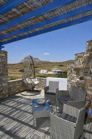 A covered outdoor seating area with wicker furniture, a hanging chair, and a view of the landscape.