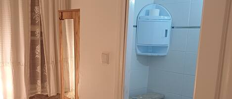 A bathroom with a toilet, a towel, a soap dispenser, and a shower curtain.