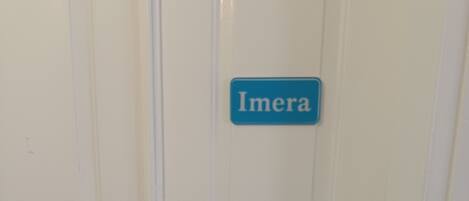 Una puerta blanca con un letrero azul que dice 'Imera' y un picaporte plateado.