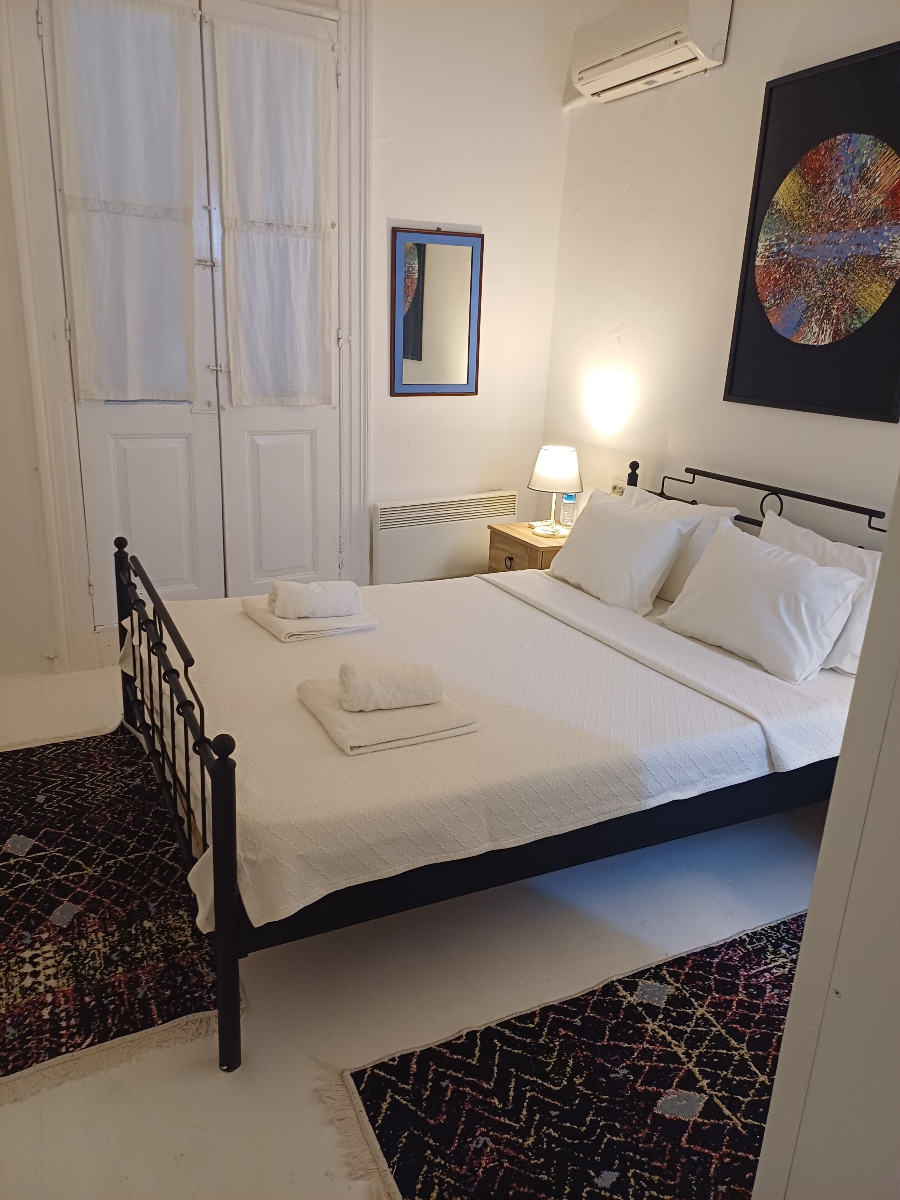A bedroom with a bed, a nightstand, a lamp, a mirror, and a door with curtains.
