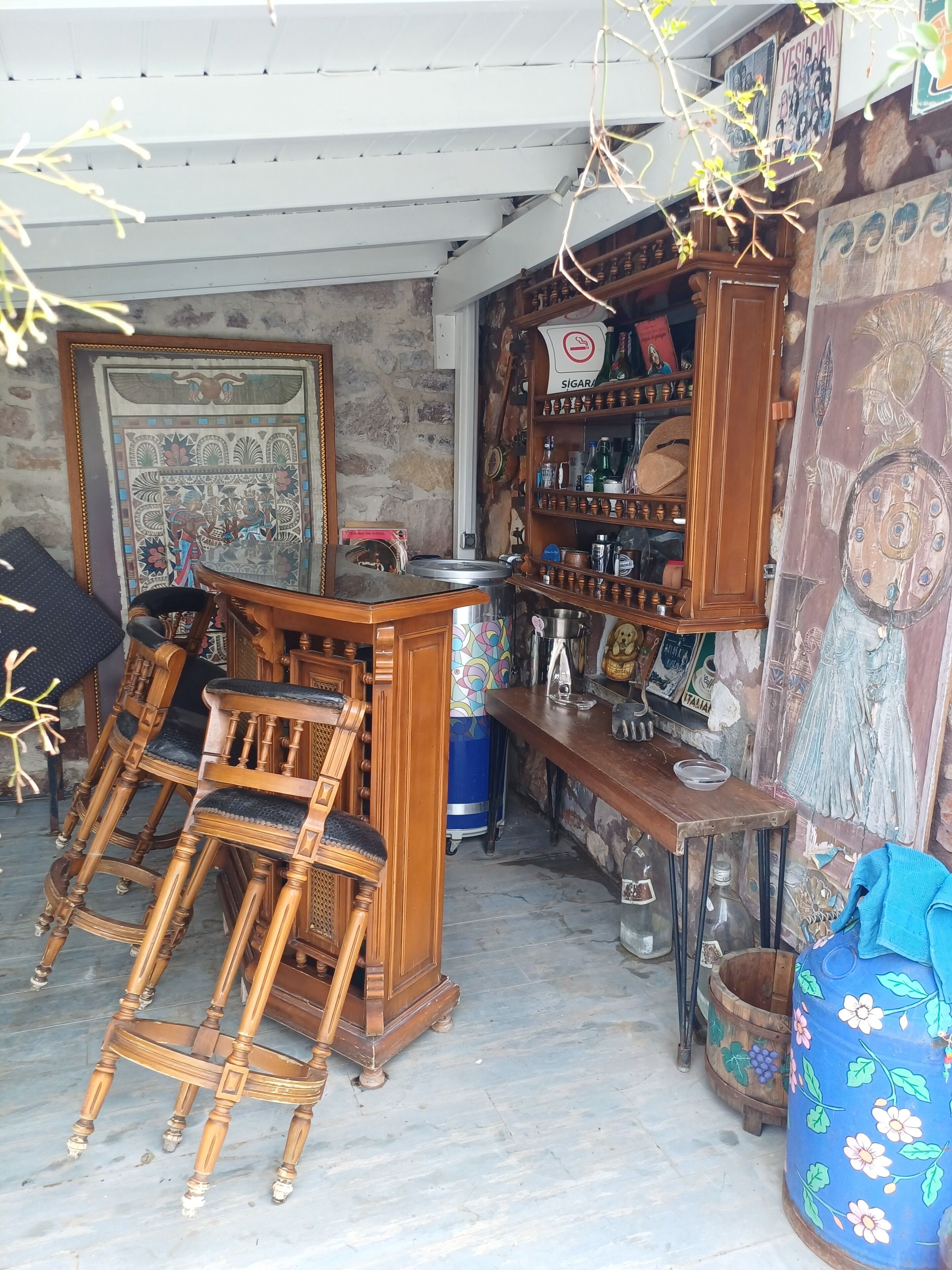 Una habitación con barra de madera, sillas, un barril azul y un muro con un mural.