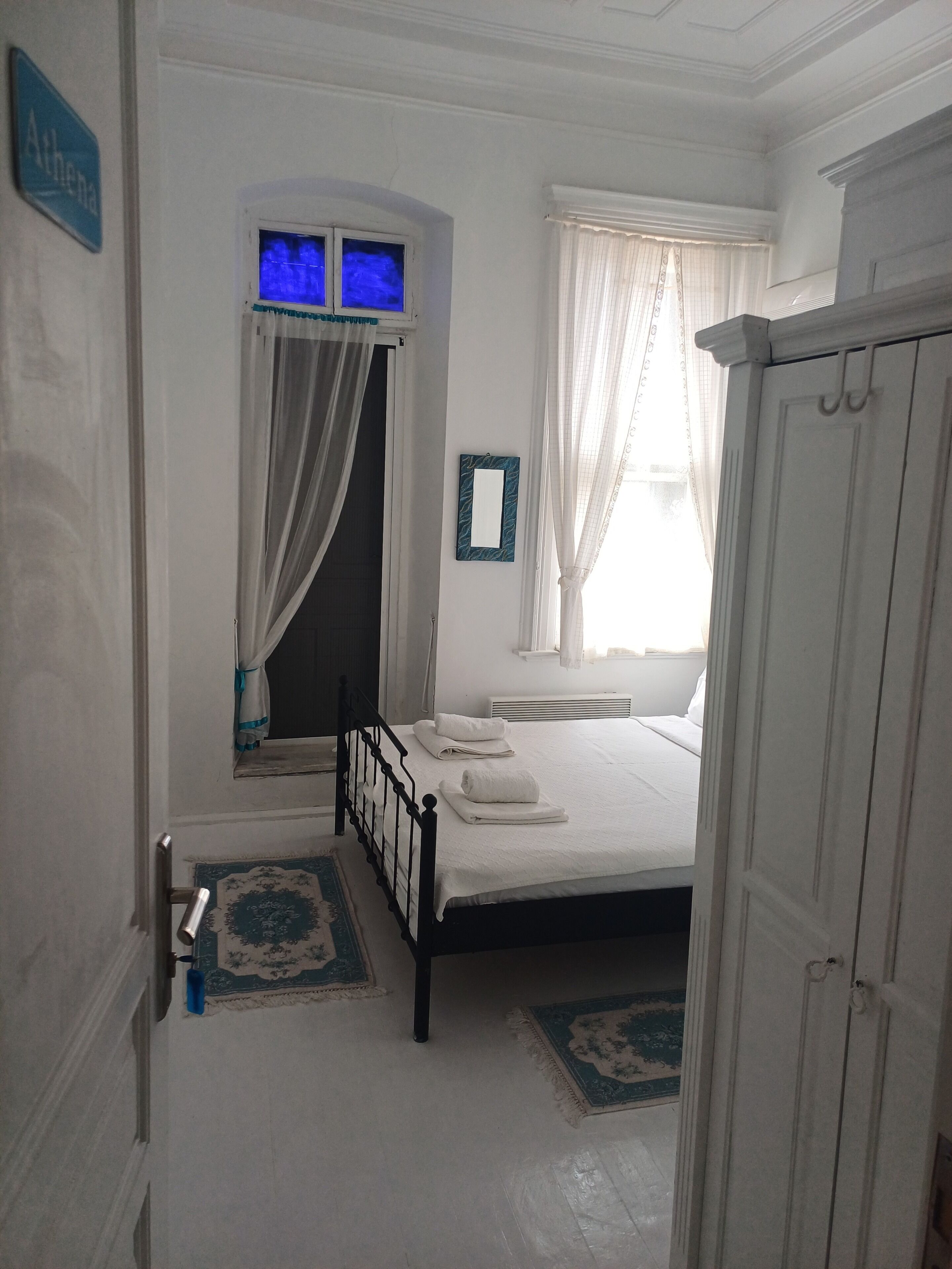 A bedroom with a bed, a window with curtains, a door, and a small rug.